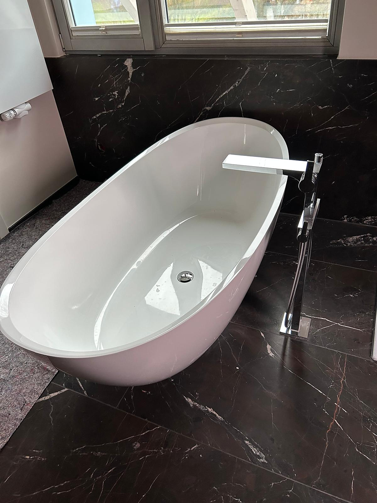Freistehende Badewanne mit Standarmatur vor dunklen Marmorfliesen