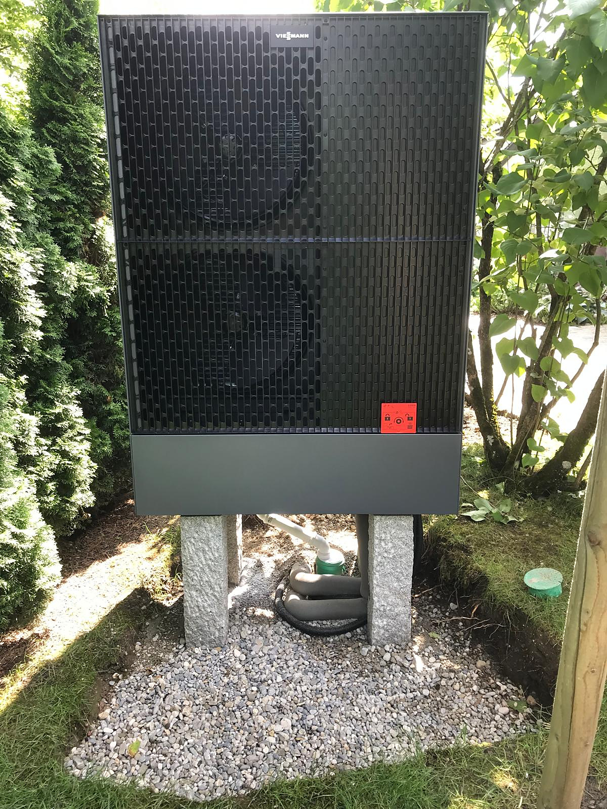 Viessmann-Wärmepumpe auf Granitsockeln im Garten mit Kiesbett und Kondensatablauf